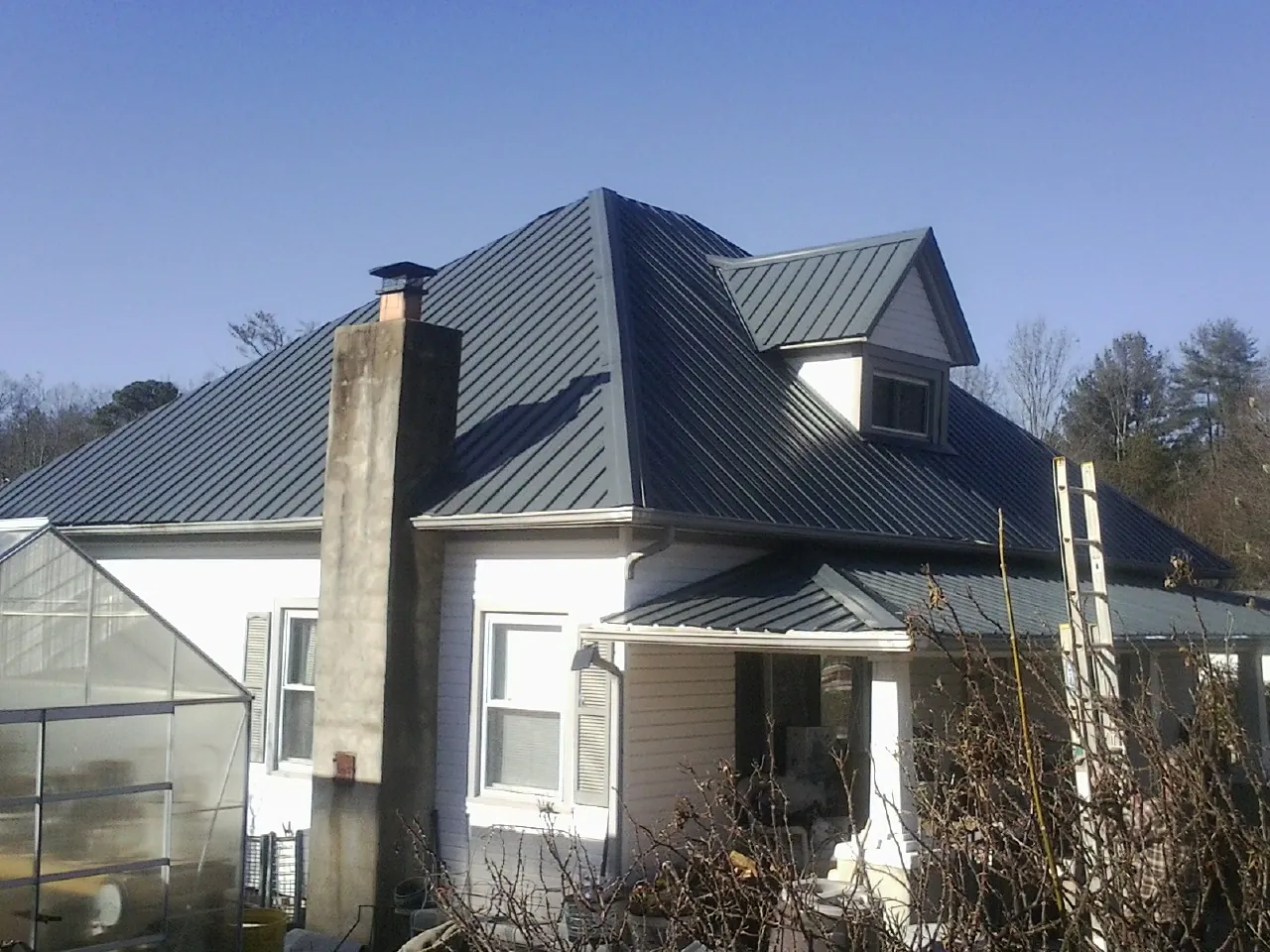 Dark blue standing seam metal roof on a white farmhouse with dormer — Slate & Tile Roof Repair by Roofing Brothers in Louisville