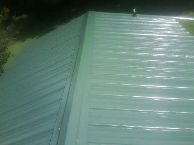 New green metal panels meeting at the ridge of a roof — Flat Roof Repair work by our crew in Louisville